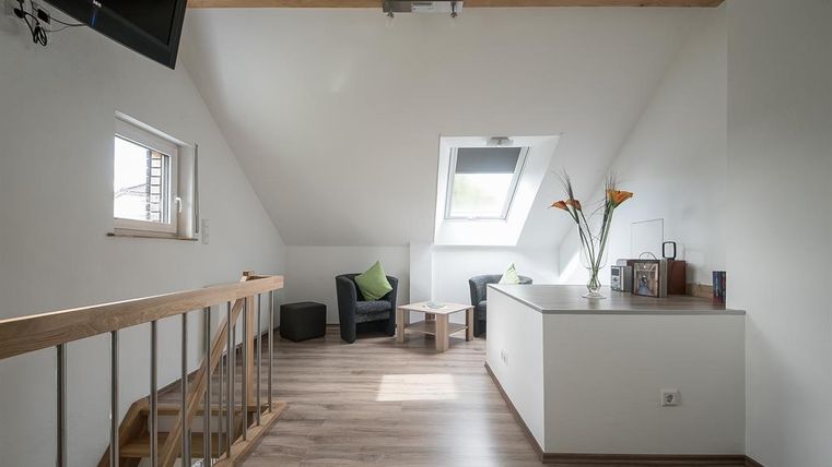 Une pièce lumineuse et moderne avec des fenêtres de toit et un plafond en bois. Il y a deux fauteuils confortables et une petite table.