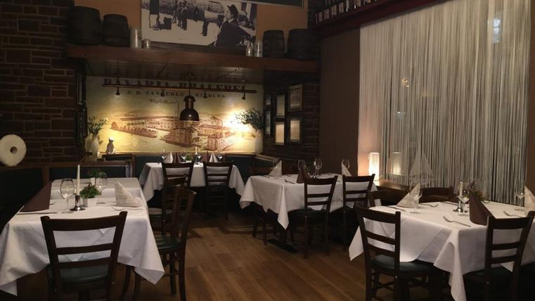 Ein gemütliches Restaurant mit eleganten Tischen und Stühlen. Die Wände sind mit Bildern und Weinflaschen dekoriert.