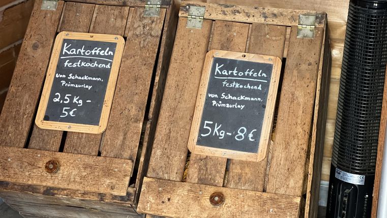 Two wooden crates with potatoes stand next to each other. Each sign displays the price for 2.5 kg and 5 kg of potatoes.