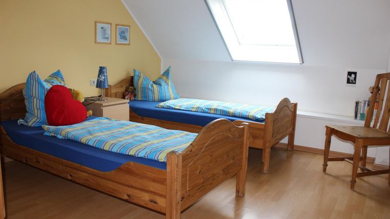 Een gezellige slaapkamer met twee eenpersoonsbedden en kleurrijke beddengoed. De kamer heeft een heldere sfeer met een dakraam en een stoel in de hoek.