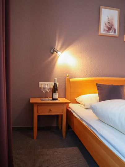 Une chambre confortable avec un lit en bois et une table de nuit. Sur la table de nuit, il y a deux verres et une bouteille de vin.