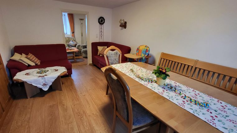 A cozy living space with two red sofas and a wooden dining table. A beautiful tablecloth and a plant are on the table.