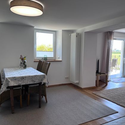 Ein helles und einladendes Esszimmer mit einem Tisch und Stühlen. Große Fenster lassen viel Tageslicht herein und bieten einen Blick nach außen.