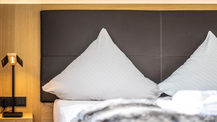 Une chambre moderne avec un grand lit et des coussins élégants. À côté du lit se trouve une lampe de chevet élégante.