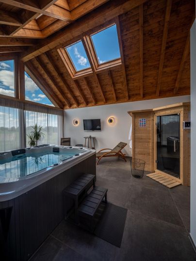 Ein moderner Wellnessbereich mit einem Whirlpool und einer Sauna. Große Fenster lassen viel Licht herein und sorgen für eine entspannende Atmosphäre.