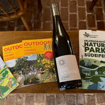 Une bouteille de vin est posée sur une table à côté de plusieurs brochures sur des destinations de voyage. Les brochures présentent différentes régions et des activités en plein air.
