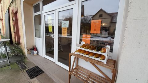 A shop with large windows that displays a range of bottles on a wooden rack. Several pieces of information are hanging at the door on yellow notes.