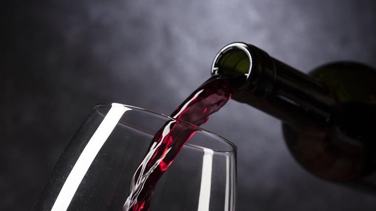 Ein Glas Rotwein wird aus einer Flasche eingeschenkt. Der Hintergrund ist dunkell und sorgt für eine elegante Stimmung.