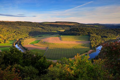 Landschaft mit Fluss, Feldern und Wäldern bei Sonnenuntergang.