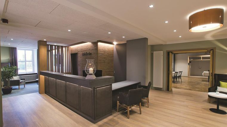 A modern reception area with a minimalist reception desk and comfortable seating. The walls are painted in soft colors and the floor is made of light wood.