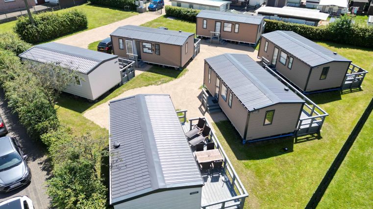 Un groupe de maisons de vacances sur un terrain verdoyant. Les maisons sont modernes et bien disposées, entourées d'arbres et de pelouses.