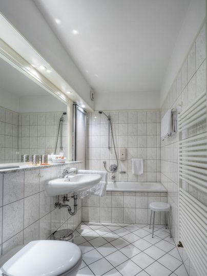 Ein modernes Badezimmer mit weißen Fliesen und einer Dusche. Es gibt ein Waschbecken, einen Spiegel und Handtücher.