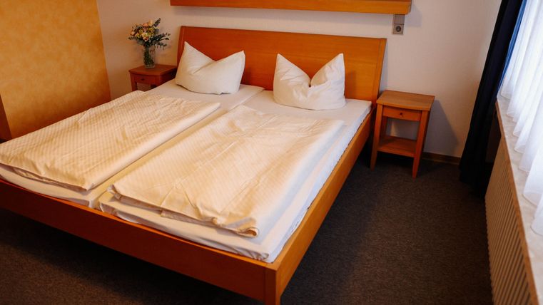 Une chambre confortable avec un lit double et deux oreillers. À côté du lit se trouve une table de nuit et il y a un bouquet de fleurs sur le rebord de la fenêtre.