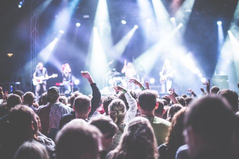 Ein energiegeladenes Konzert mit einer begeisterten Menge. Die Band spielt auf einer Bühne, umgeben von buntem Licht.
