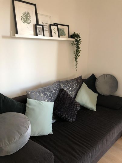 Eine elegante Couch mit verschiedenen Kissen in sanften Farben. Im Hintergrund hängen Bilder an der Wand und eine Pflanze ist dekorativ platziert.