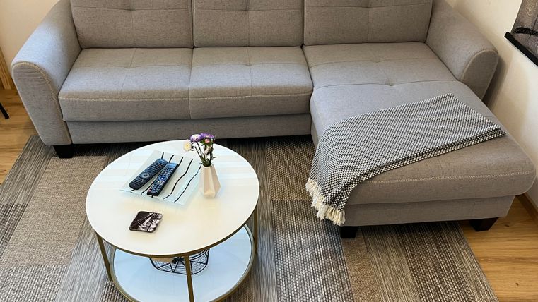 Un canapé gris moderne avec un coin se trouve dans le salon. Devant le canapé, il y a une table ronde avec un petit vase et divers objets.