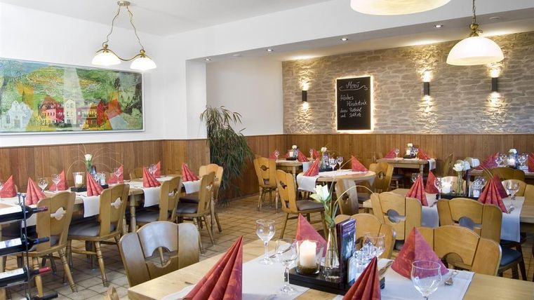Een uitnodigend restaurant met houten decor en stijlvolle placemats. Rode stoffen servetten en mooie bloemarrangementen zorgen voor een gezellige sfeer.
