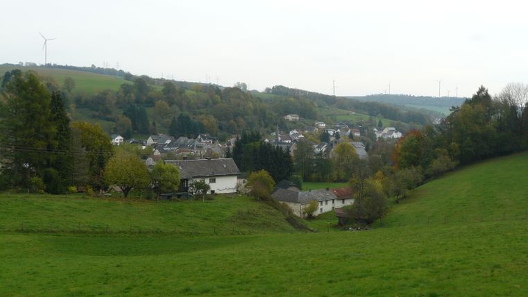 Landschapsgezicht van Mettendorf met huizen en windturbines op de achtergrond.