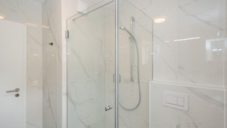 Une douche moderne avec des portes en verre et un design de carreaux marbré clair. La pièce a l'air propre et élégante.