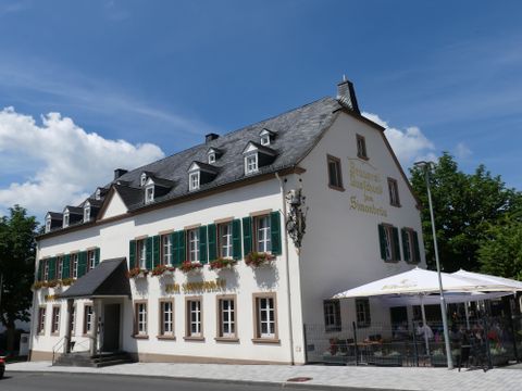 Ein charmantes, zweigeschossiges Gebäude mit grünen Fensterläden. Draußen gibt es eine Terrasse mit Sonnenschirmen.