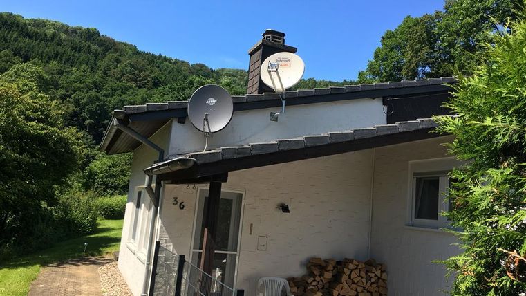 Une maison confortable avec des paraboles et un joli jardin. En arrière-plan, on peut voir des collines verdoyantes.
