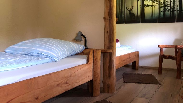 A Twinbed-room with two wooden beds and a chair. A picture of a forest hangs on the wall.
