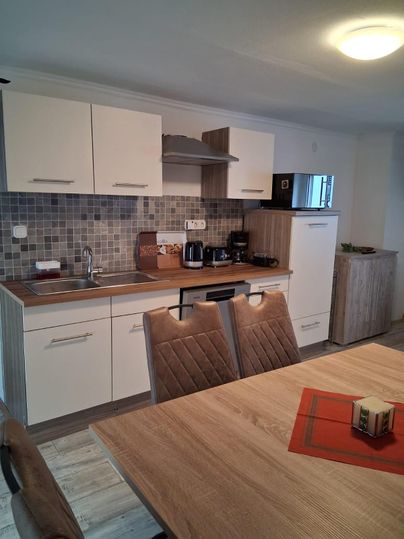 Une cuisine moderne avec des meubles clairs et une surface en bois élégante. La table est décorée d'un sous-verre rouge et en arrière-plan, divers appareils de cuisine sont présents.