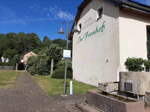Ein gemütliches Gasthaus mit dem Namen "Im Frohnhof" und einem begrünten Außenbereich. Im Hintergrund sind Bäume und eine blaue Himmel zu sehen.