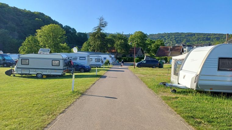 Een parkeerplaats voor campers met een brede straat in het midden. Omgeven door groene weilanden en bomen.