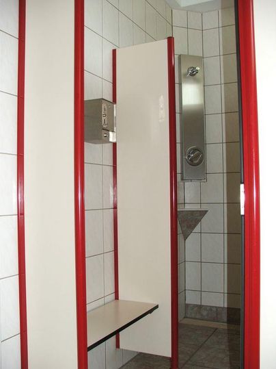 Une cabine de douche avec des carreaux gris et des accents rouges.
Sur le mur, il y a un support et une étagère.