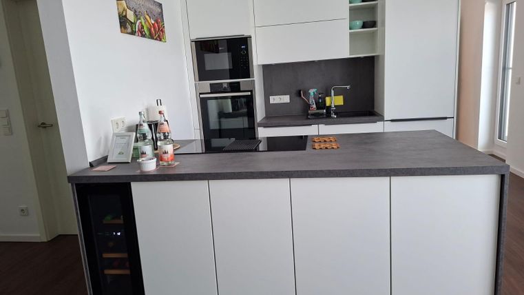 A modern kitchen with white furniture and a wooden countertop. It is well equipped with a stove, an oven, and a sink.