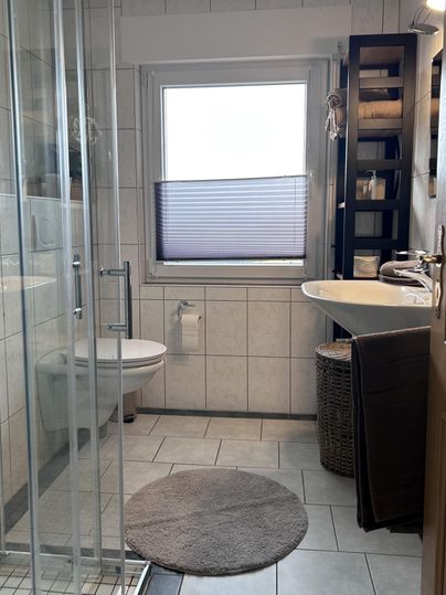 Een moderne badkamer met een douche, een wastafel en handige opbergvlakken. De ruimte is helder en vriendelijik ingericht.