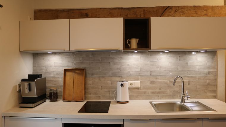 Une cuisine moderne avec des armoires claires et un plan de travail élégant. Les murs sont décorés de carreaux gris et l'éclairage crée une ambiance agréable.