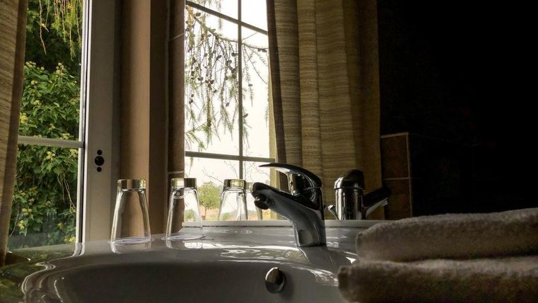 Une salle de bain élégante avec un lavabo et un robinet moderne. Par la fenêtre, un paysage de plantes vertes est visible.