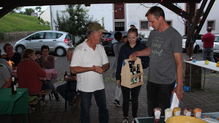 Een groepsactiviteit in de buitenlucht met meerdere personen. Twee mannen en een meisje staan in het middelpunt en houden een geschenkdoos vast.