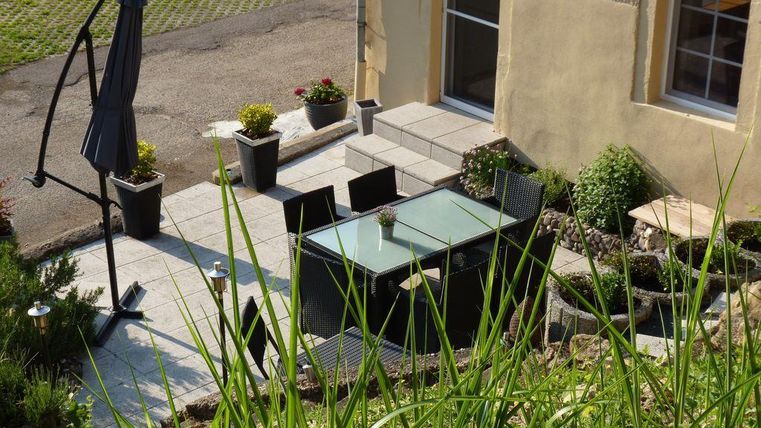 An inviting outdoor area with a garden table and chairs. Surrounded by plants and a sun umbrella stand.