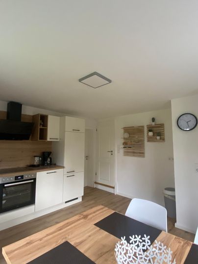 Eine helle Küche mit modernen Schränken und einem Esstisch. Auf dem Tisch steht eine dekorative Schüssel.