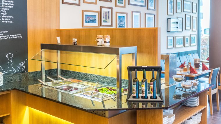 Een uitnodigende eetruimte met een saladbuffet en houten planken. Aan de muur hangen verschillende afbeeldingen die een gezellige sfeer creëren.