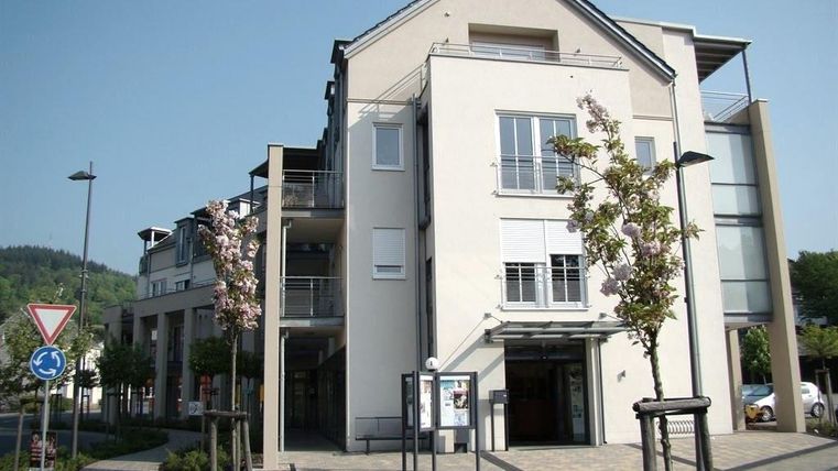 Een modern gebouw met heldere lijnen en grote ramen. Voor het gebouw zijn beplante oppervlakken en een kleine straat zichtbaar.