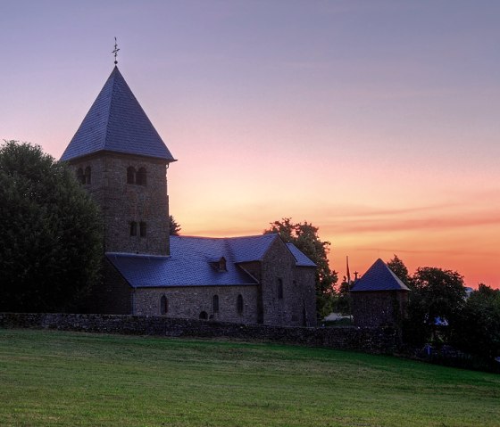 Eine Kirche mit Turm vor einem farbenfrohen Sonnenuntergang, umgeben von Bäumen und einer Wiese., © Naturpark Südeifel, C. Schleder