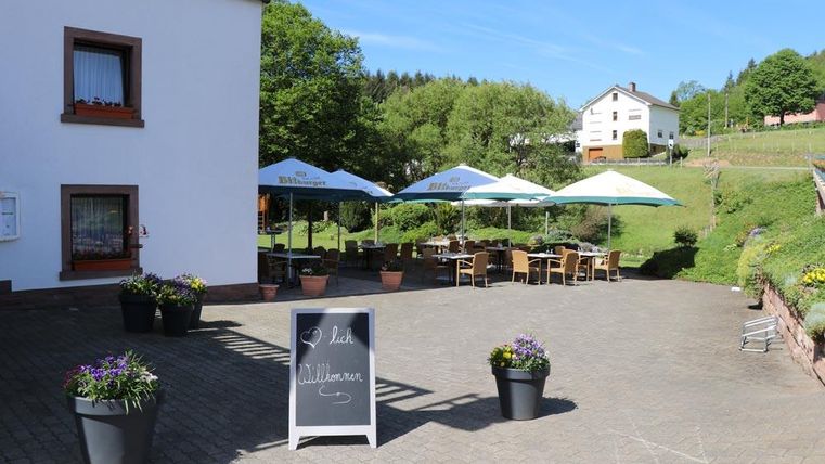 Un espace extérieur accueillant avec des tables et des parasols. Entouré de collines verdoyantes et de fleurs en pots.