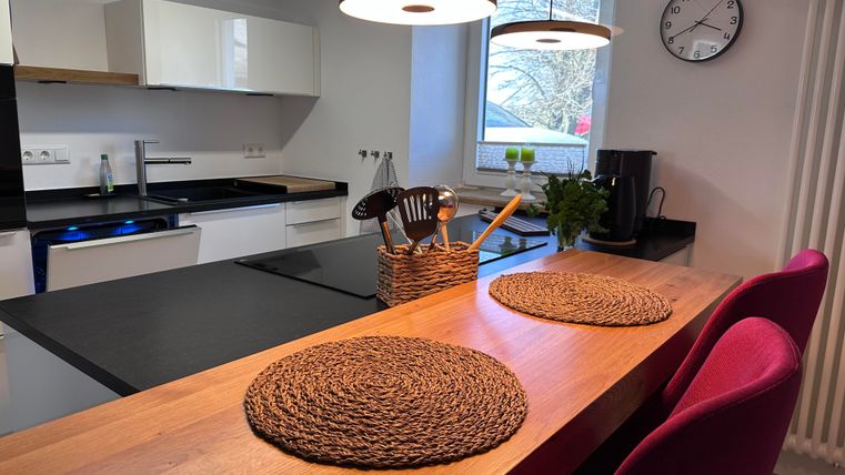 Eine moderne Küche mit einem Holzarbeitsplatten und eleganten Möbeln. Auf dem Tisch liegen Platzsets, und es gibt viel Tageslicht von einem Fenster.