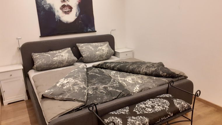 Une chambre moderne avec un grand lit et une literie grise élégante. Au mur, une œuvre d'art représentant un visage est accrochée.