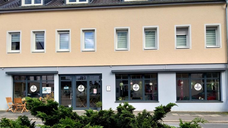 Een modern kantoorgebouw met een lichte gevel. Voor het gebouw staan enkele meubels en er zijn grote ramen met uitnodigende borden.