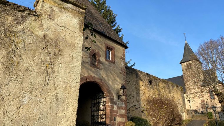 Ein historisches Tor mit einer steinernen Mauer und einem daran angrenzenden Turm. Der Himmel ist klar und blau.