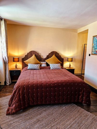 Een gezellige slaapkamer met een groot, bruin bed en gele kussens. Zacht licht van de nachtlampjes zorgt voor een ontspannen sfeer.