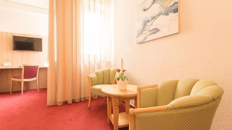 Un espace de vie confortable avec deux fauteuils et une petite table. De rideaux clairs laissent entrer beaucoup de lumière du jour.