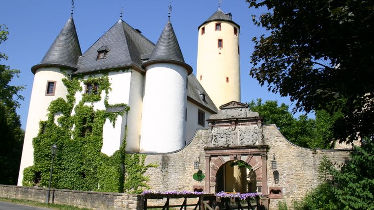 Burg Rittersdorf mit Türmen und Torbogen, umgeben von Bäumen.