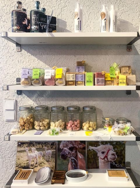 Een rek met verschillende producten, waaronder glazen met kleurrijke lekkernijen en kruiden. Op de onderste plank zijn ook foto's van dieren en kleine utensiliën te zien.