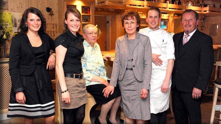 Un groupe de six personnes se tient dans un restaurant. Elles sourient amicalement et posent ensemble pour la photo.